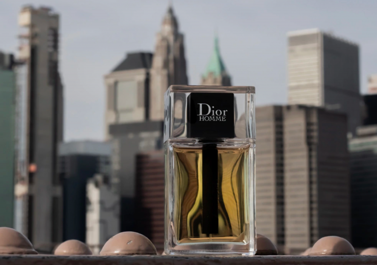 Il flacone di Dior Homme in primo piano su una trave metallica del ponte di Brooklyn, con lo skyline di New York sullo sfondo
